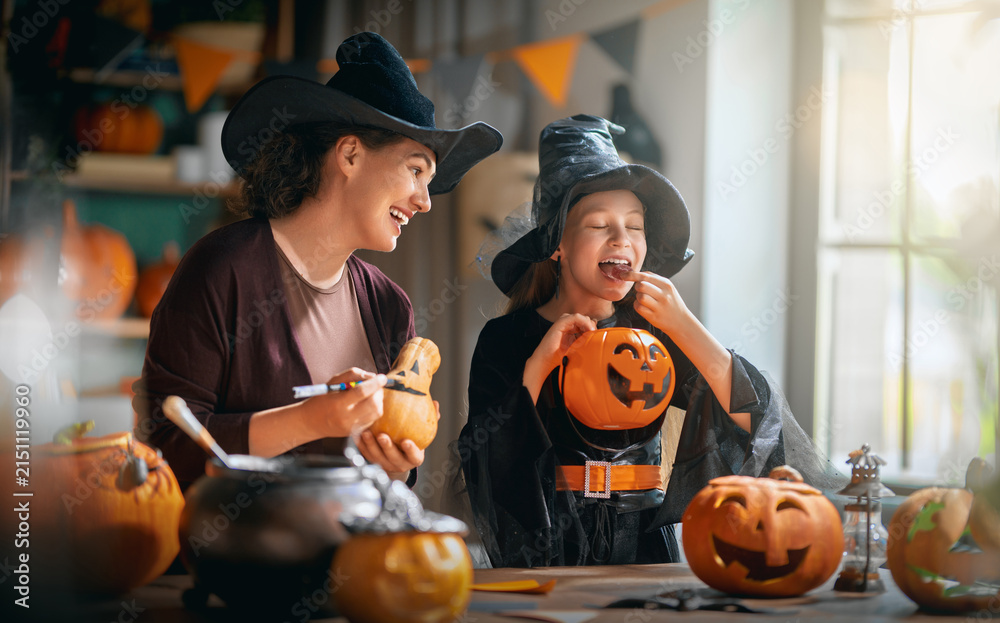Obraz premium Happy Mother and Daughter in Witch Costumes Carving Pumpkins