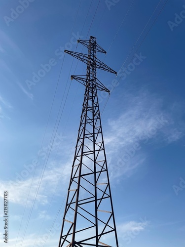 High Voltage Electric Power Transmission Tower Against a Clear Blue Sky with Soft Clouds