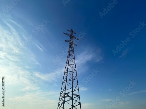 High Voltage Electric Power Transmission Tower Against a Clear Blue Sky with Soft Clouds