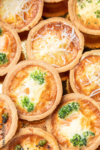 Obraz na plátne Assorted mini quiches with broccoli, cheese, and vegetables on a golden backgrou