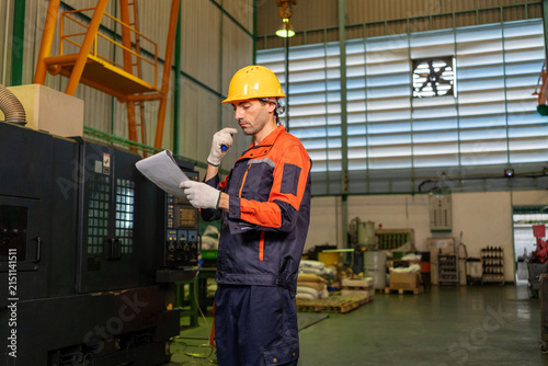 Engineer factory worker helmet uniform machine document radio industrial safety male technician reading checklist near equipment factory workshop