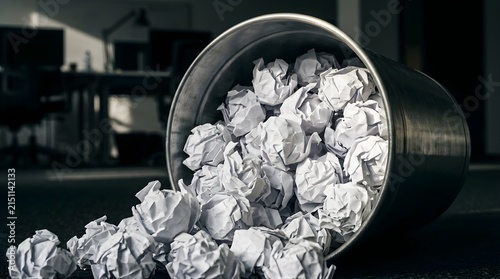 Metal waste bin overflowing with crumpled paper balls in an office room