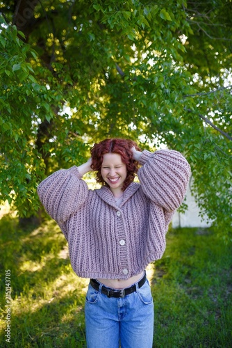 Foto Young smiling girl with curly red hair in chunky knit sweater with hood outdoors