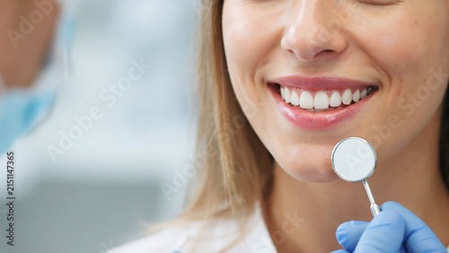 Woman smiling widely during dental examination with professional dentist using dental mirror tool