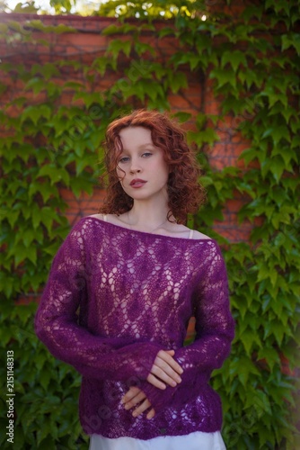 Redhead teenager girl model in knitted purple transparent sweater and white silk skirt posing outdoors. Clothing and fashion concept