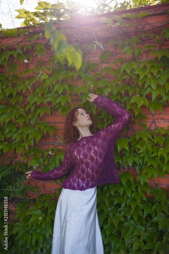 Redhead teenager girl model in knitted purple transparent sweater and white silk skirt posing outdoors. Clothing and fashion concept