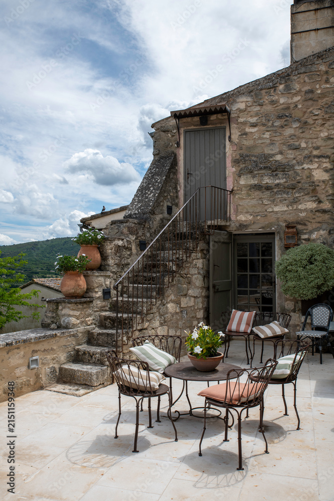 Naklejka premium Sunny Outdoor Terrace With Table And Chairs Beside A Rustic Stone Building Overlooking Countryside