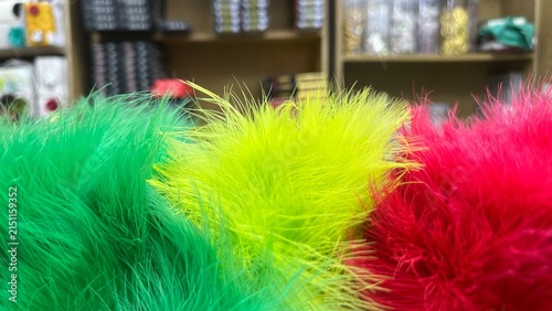 A vibrant close-up macro shot featuring fluffy, brightly dyed green, yellow, and red feathers or long-pile faux fur creating a soft, colorful, and playful abstract texture.