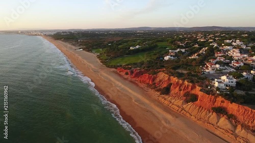 Golden hour aerial footage flying along the stunning vale do lobo coastline. Showing the vast sandy beach. Red sandstone cliffs. And luxury villas nestled amongst green golf courses in algarve
