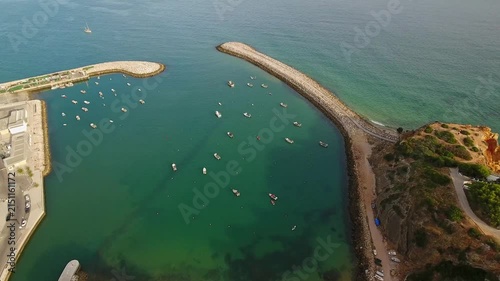 Stunning aerial perspective capturing the entrance to albufeira marina, where numerous boats are anchored in the calm, emerald waters of the algarve coastline during a beautiful sunny day
