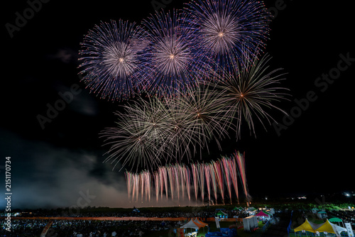 Row of blue-white fireworks blooming side by side over festival crowd