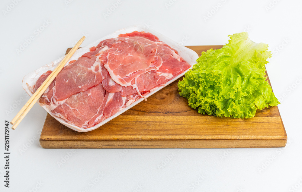 Fototapeta premium Sliced raw meat in tray with green lettuce and chopsticks on wooden board isolated on white