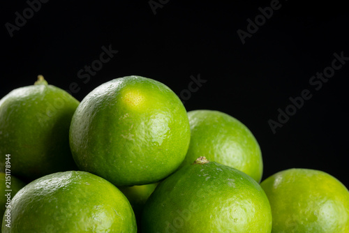 Pile of whole fresh green key limes on black background