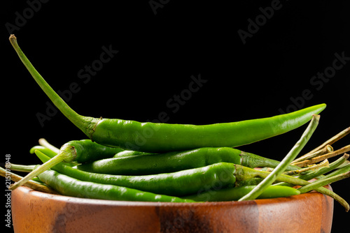 Pile of fresh green Thai Jinda chili peppers in brown wooden bowl on black background.
