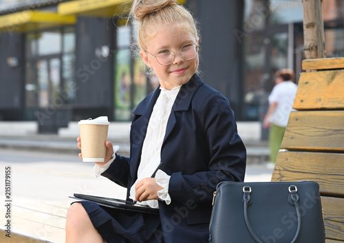A little girl, elegantly dressed in a business suit, smiles at the camera