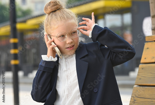 A little girl dressed in a business suit is talking animatedly on a smartphone