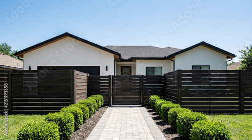 Modern white stucco house with dark wood slat fence and manicured hedges, sunny day, suburban real estate, home exterior