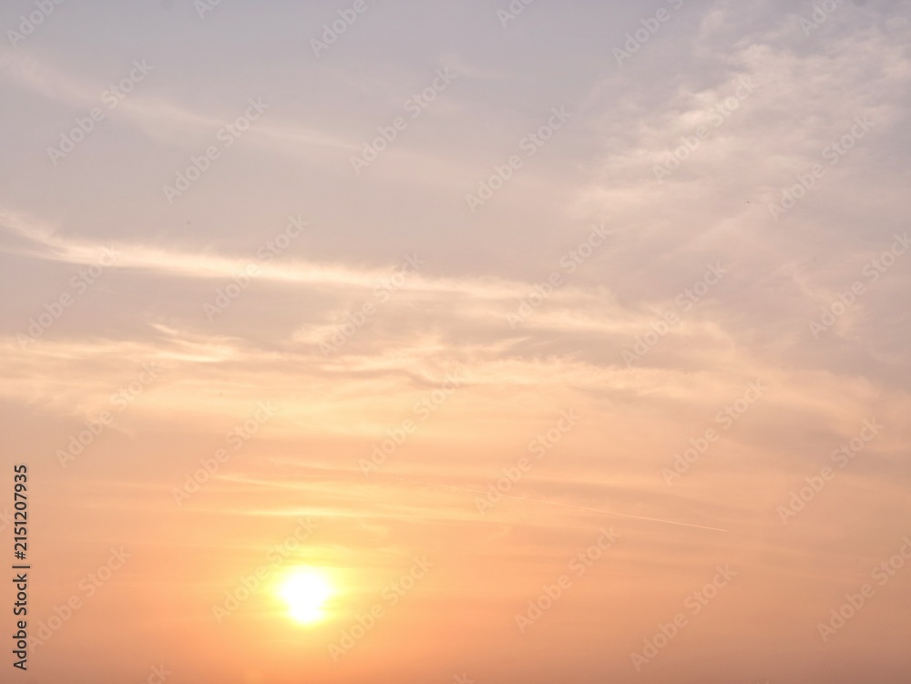 Fototapeta premium Beautiful soft pastel sky with the sun setting, casting warm orange and pink hues on wispy cirrus clouds. A peaceful natural background for various creative projects