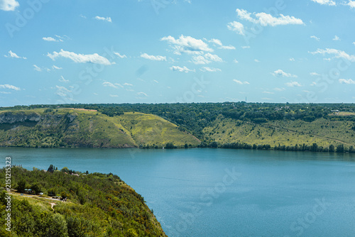 Expansive blue river flows through rolling green hills under a bright summer sky
