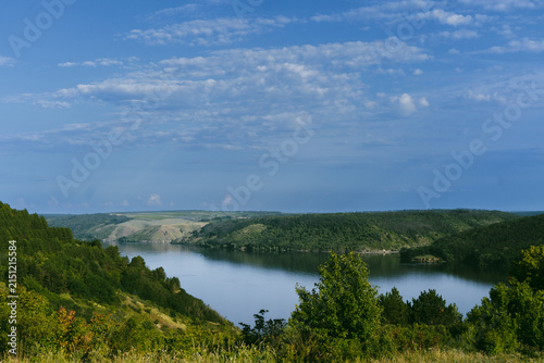 Expansive river valley landscape with lush green hills and a calm blue sky
