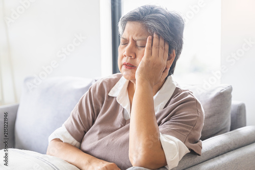 Sick, stress caucasians senior. Mature, adult elderly woman having migraine pain, headache symptom, feeling unhealthy, suffering from dizzy when sitting on sofa. Health care problems of older people.