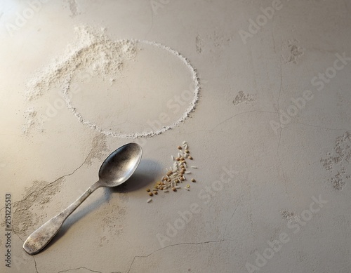 Silver spoon with flour circle and grains on concrete