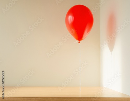 Red balloon floating in minimalist room casting shadow