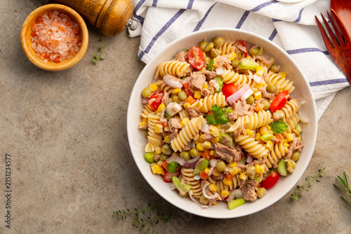 Homemade macaroni salad with Fusilli Pasta and canned tuna, carrot, onion, corn, tomato, green peas and mayonnaise dressing in a white plate on wooden table.Top view.