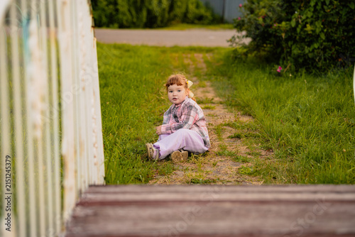 Little girl sitting on a path in a park. Cute child enjoying a sunny day outdoors in nature. Summer leisure time, childhood lifestyle, outdoor activity, and exploration concept.