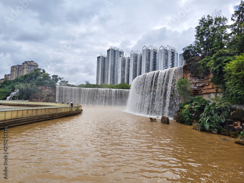 Wide view of the giant artificial waterfall and pedestrian bridge at Kunming Waterfall Park in Yunnan Province. KUNMING, YUNNAN, CHINA - JULY 31, 2026.