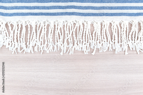 A blue and white striped blanket with fringed edges. On a wooden table.