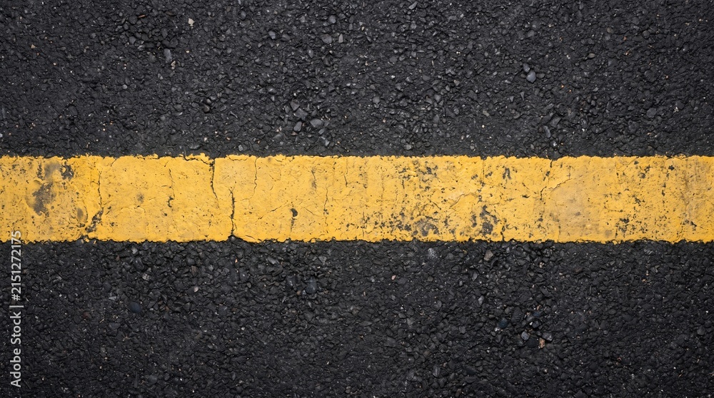 Fototapeta premium Worn yellow dividing line on black asphalt road surface texture