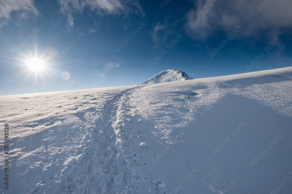 Obraz premium Snowy Route Path With Footprints Leading Towards Mont Blanc Summit 4810m Peak In Background Under Bright Sun Blue Sky High Altitude Alpine Expedition In French Alps Chamonix Outdoor Trekking Hike