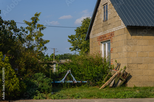 Rural farm building with concrete block wall, roof, and farm equipment in green yard