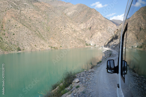 Photography A minibus driving on a dusty road near lake in the Asian mountains