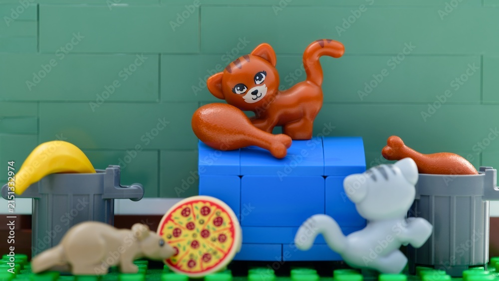 Fototapeta premium Tambov, Russian Federation - August 03, 2026 A close-up shot of Lego cats and rat minifigure searching for food like pizza and chicken near trash cans.