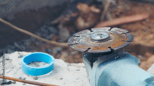 Angle grinder with blade for construction tool on concrete site while cutting disc, rusty metal equipment near worker area during builder repair work with blue plastic pipe on background.