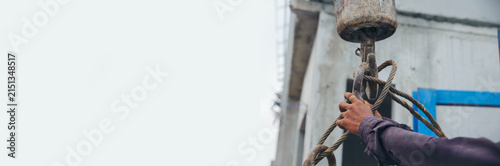 Man hand pulling metal sling of crane to lift cement platform at construction site-banner image.