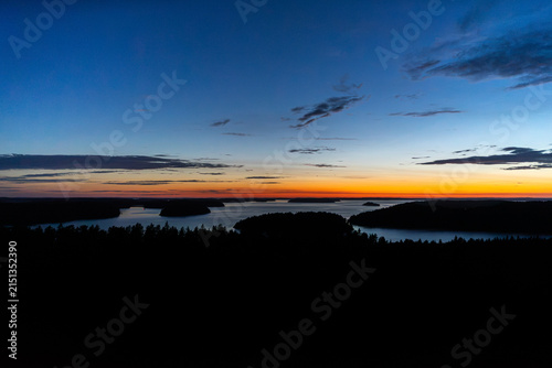 Zoom in aerial view of island during nordic summer twilight blue hour with faint yellow glow on horizon