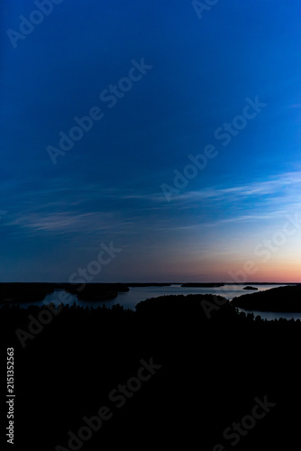Zoom in aerial view of island under rare noctilucent clouds in dark blue night sky in Finland
