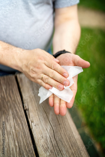 Man wiping his hands with an alcohol wipe after touching various objects outdoors. Hygiene and health protection concept.