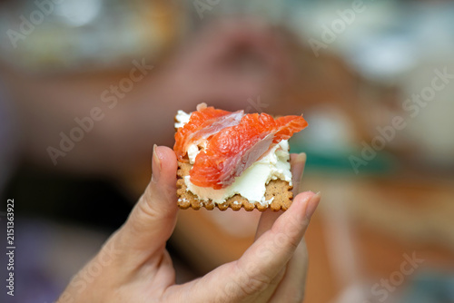 Girl's hand holding a rye crispbread with cream cheese and a piece of red salmon for breakfast. Healthy and savory morning meal.