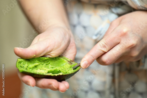 Girl's hands scooping ripe green Hass avocado flesh with a metal spoon. Healthy fruit preparation.