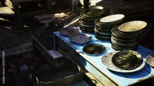 Sunlit close vignette of stacked plates and bowls on rustic bench, warm highlights and cool shadows create contrasty mood perfect for lifestyle, retail
