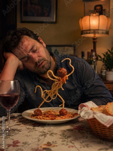 Tired man falling asleep over spaghetti and meatballs during late home dinner with wine
