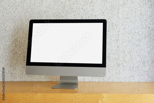 Fotografía Modern desktop computer monitor with a blank screen placed on a wooden desk against a textured white wall