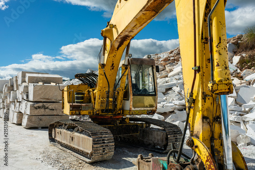 Foto Detailed look at the hydraulic systems and cabin of a massive yellow construction digger working efficiently in a natural outdoor mountainous environment to extract solid white marble materials