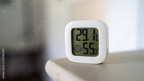 Minimal indoor climate monitor on shelf showing temperature and humidity readings in soft natural light with shallow focus, clean neutral background, modern home comfort concept