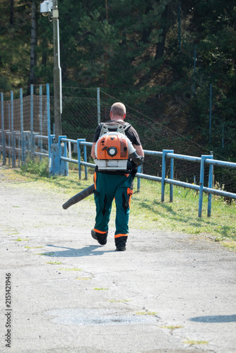 Bild auf Leinwand A water utility employee blows mowed grass away with a blower on a dam