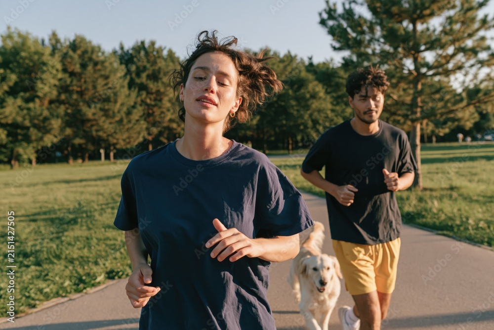 Obraz premium Active young woman and man jogging with dog on park path for fitness lifestyle background and outdoor exercise scene